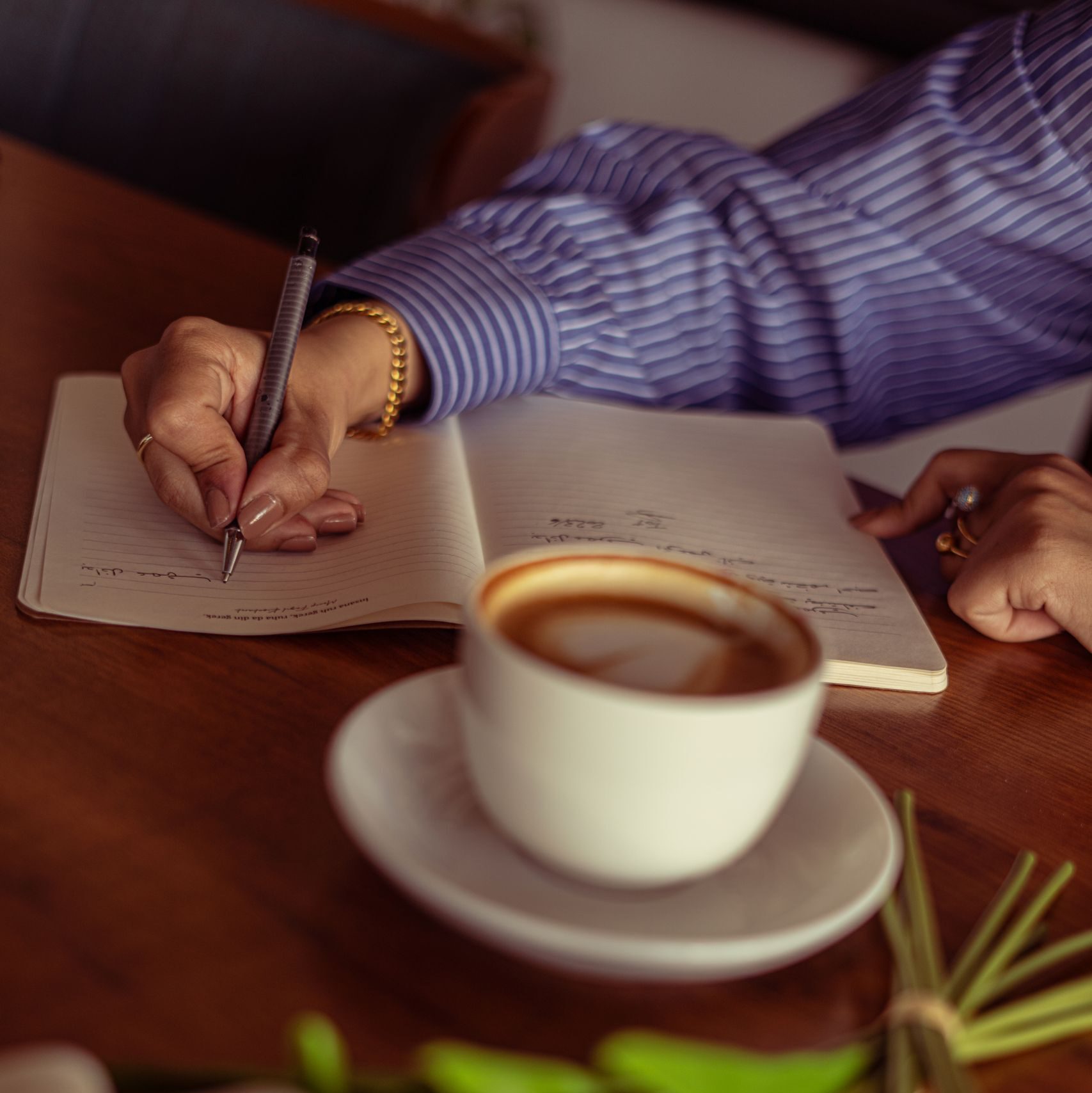 A woman writes in a journal beside a cup of coffee and white tulips.